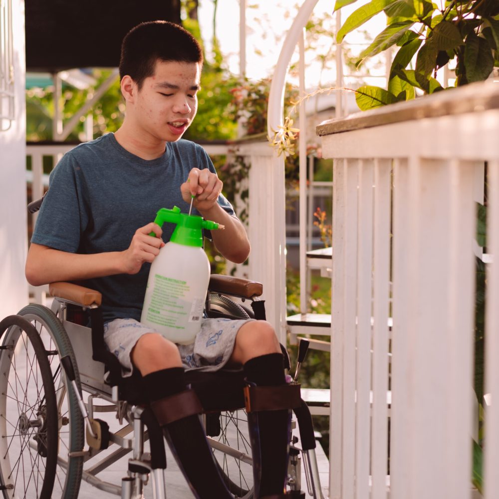 Young man with disability holding a spray bottle water the plants on a wheelchair accessible balcony,Hobby and Rehabilitation with natural therapy,Exercise relaxation,Environmentally friendly concept.